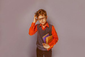 European-looking boy of ten years in glasses thinking intently book on a blue background retro