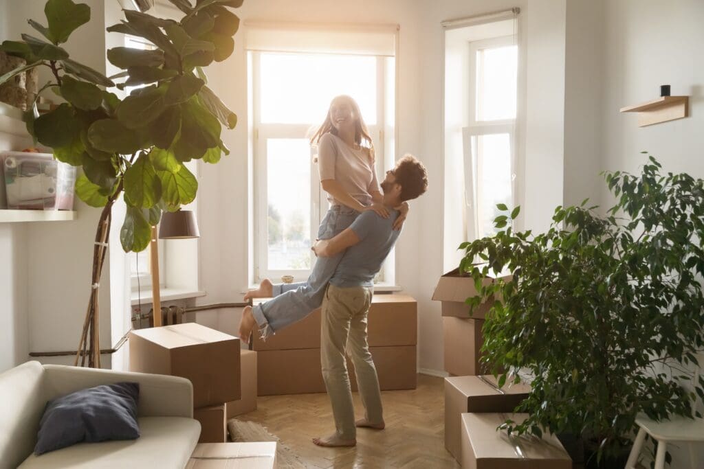 Young couple laughing together among moving boxes in the living room of their new home